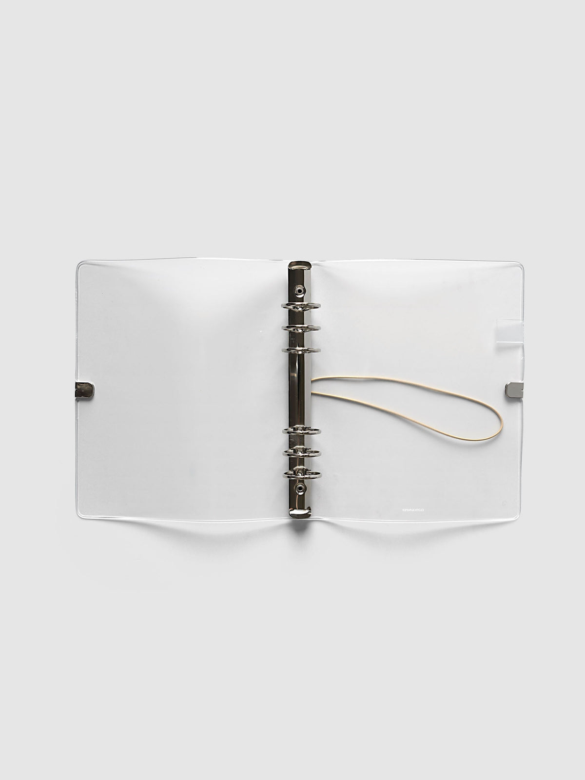 Ring Cover in frosted vinyl, A5 6-Ring Punch, open flat showing the silver six-ring mechanism, the beige bungee cord and the printed logo