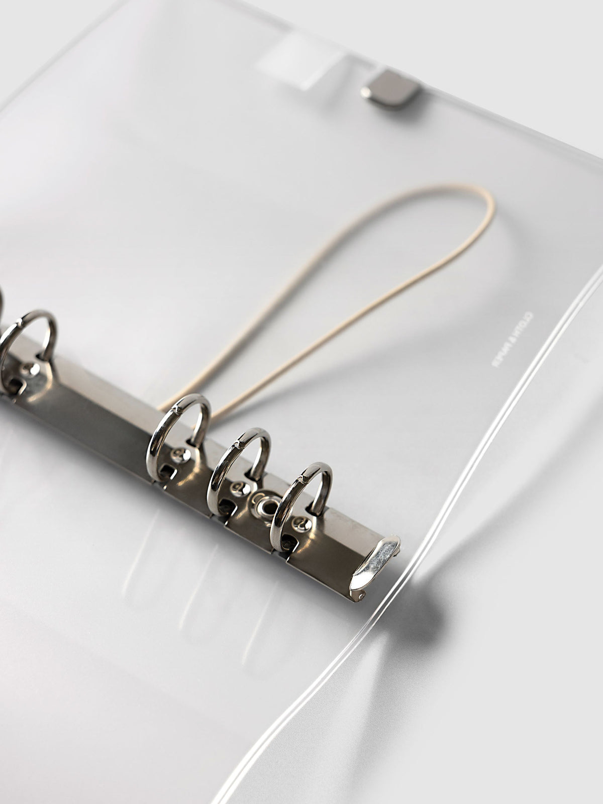 Angled close-up of the silver six-ring mechanism and beige bungee cord inside the Personal 6-Ring Punch Ring Cover in frosted vinyl