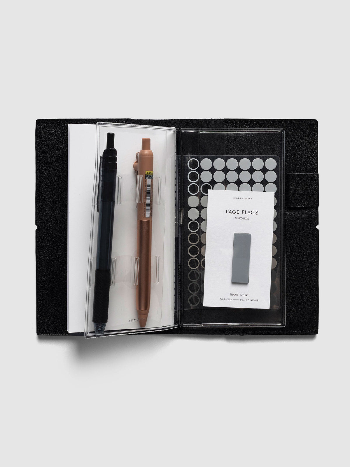 Travel Tool Kit, Pocket Plus, open inside a black travel notebook, two pens in the loops beside a pocket of dot stickers and page flags