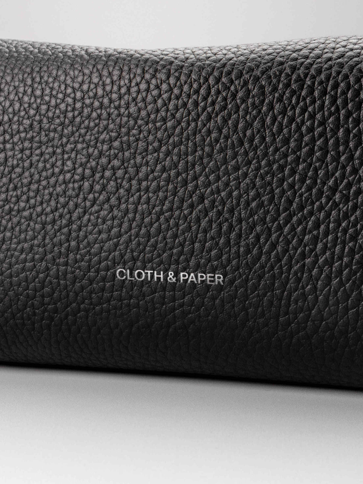 Folded Form Pouch close-up of black pebbled leather texture and silver foil Cloth & Paper logo on exterior