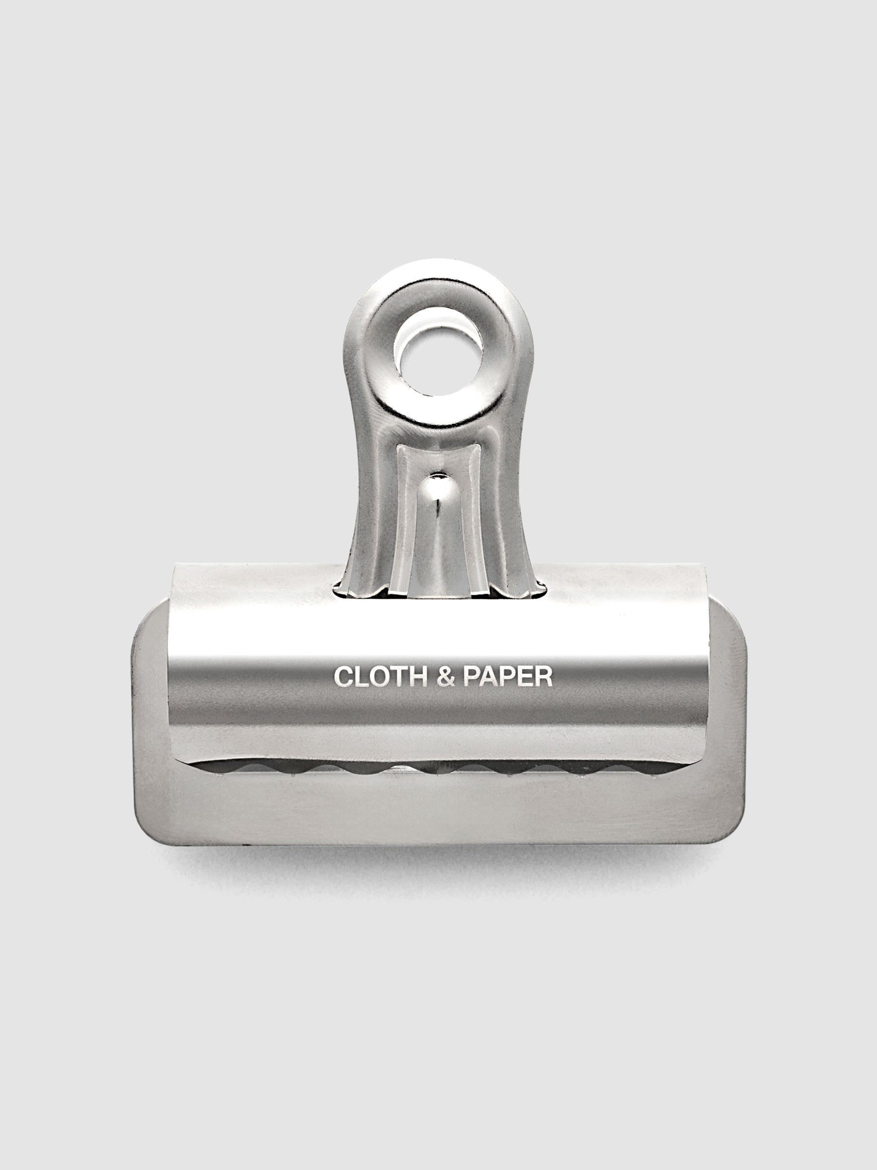 Silver metal notebook clip with Cloth & Paper logo etched onto the surface.