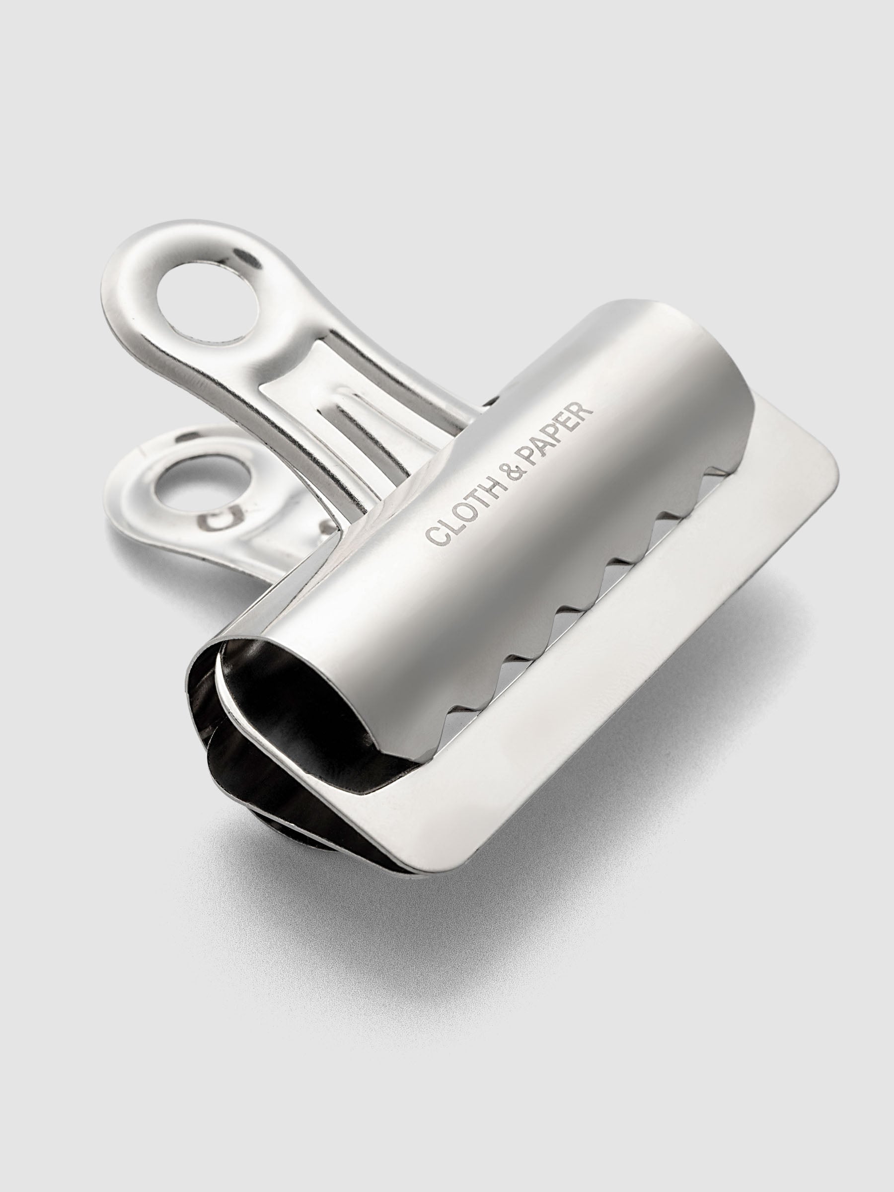 Silver metal notebook clip with Cloth & Paper logo etched onto the surface.