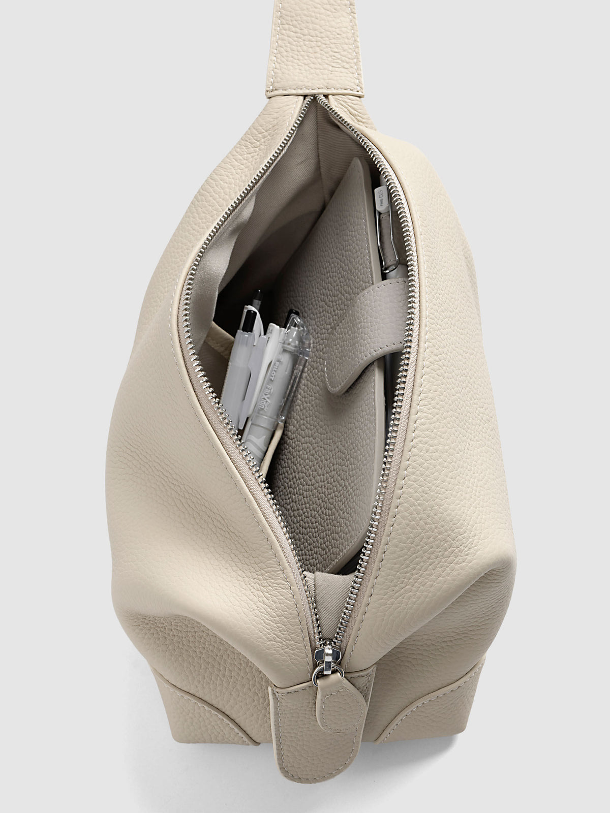 Folded Form Pouch in warm beige pebbled leather, top-down angled view, open and filled with pens and a notebook in the interior side pocket