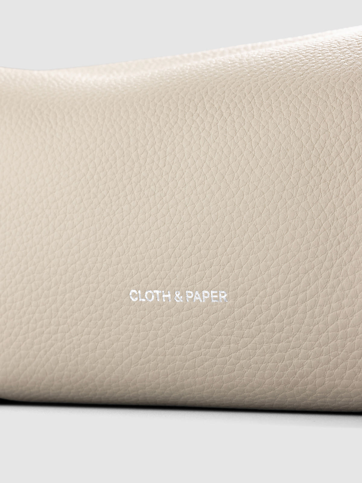 Folded Form Pouch close-up of warm beige pebbled leather texture and silver foil Cloth & Paper logo on exterior