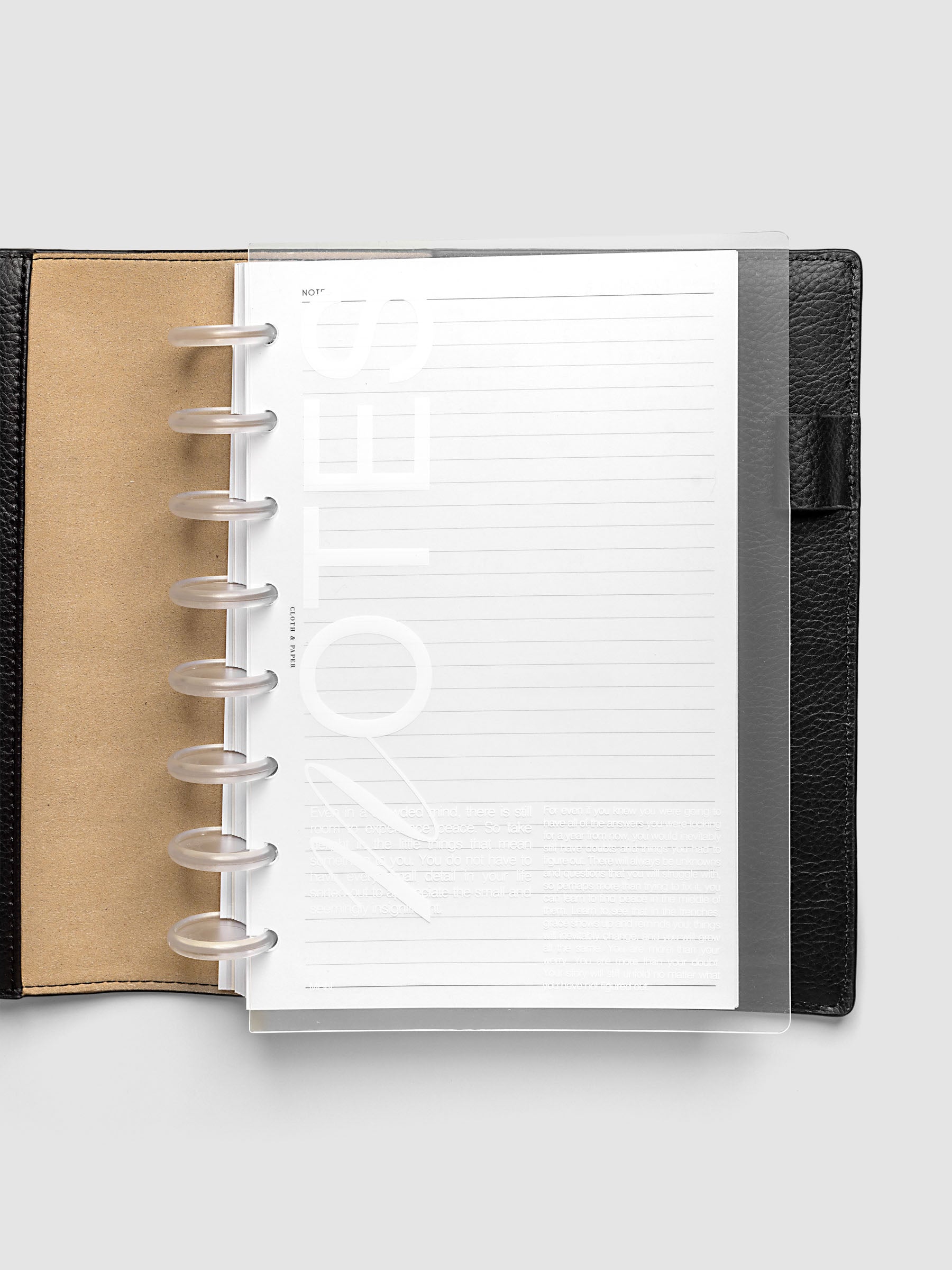 Clear plastic planner cover with white printed text shown pre-punched for Half Letter discbound planners in a black folio.