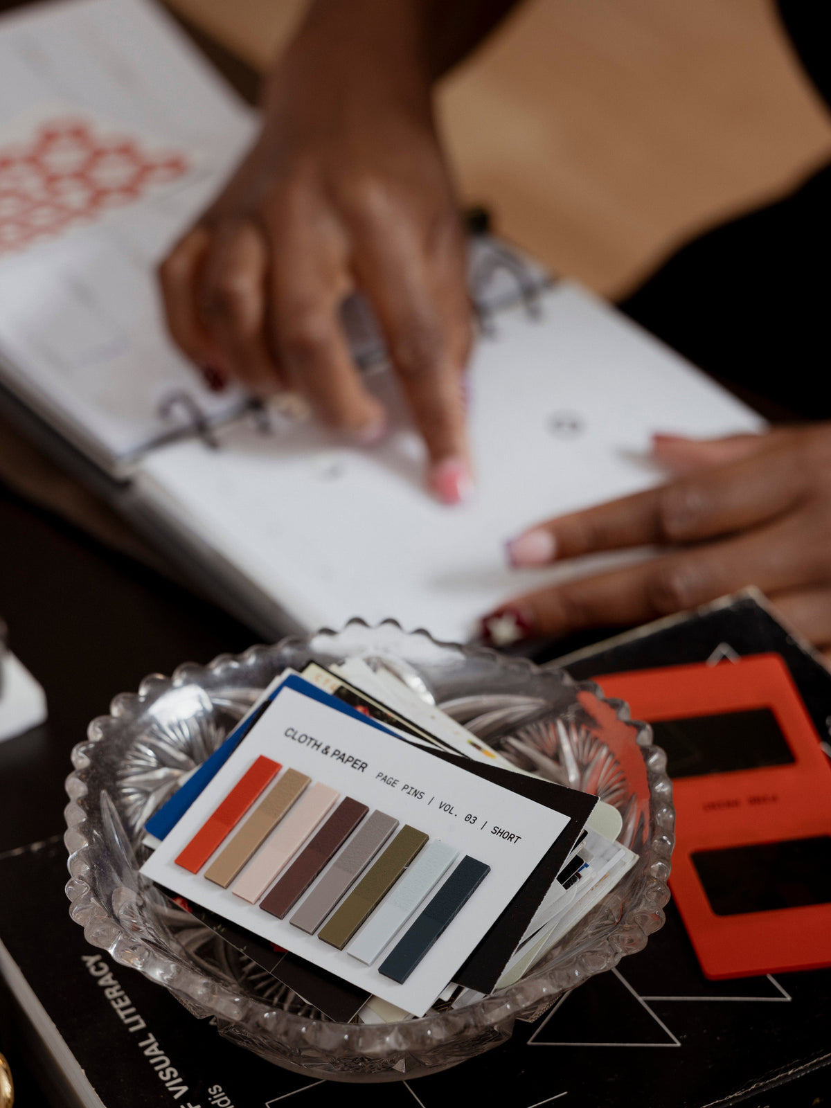 Page Pins Short on table beside woman writing in planner, eight colorways: deep orange, warm light brown, peach, burgundy, grey, olive, light blue, and navy