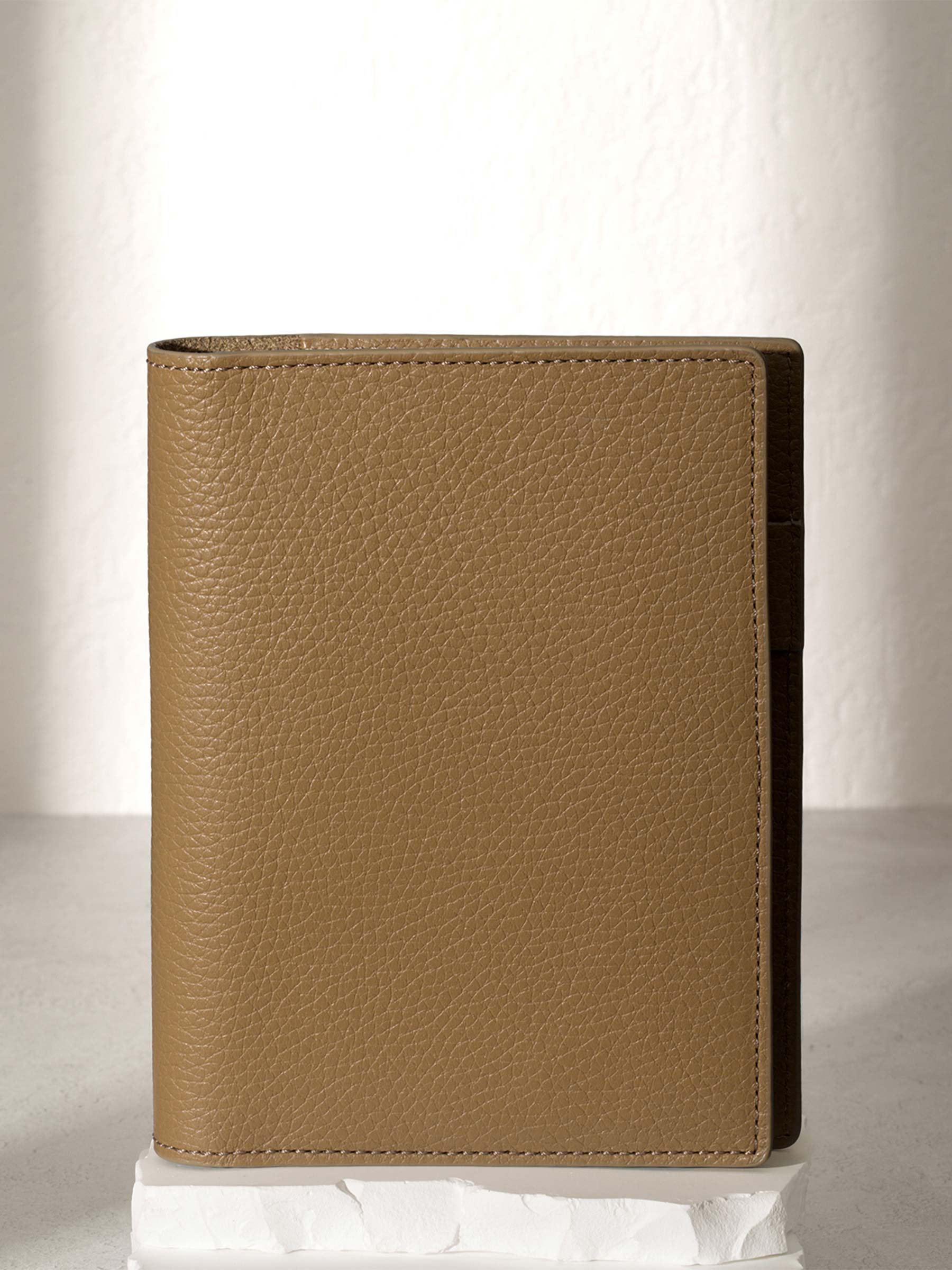 CP Petite Catalonia folio displayed on a white stone pedestal. The background is a natural textured off-white material, and a spotlight behind the folio highlights its placement.