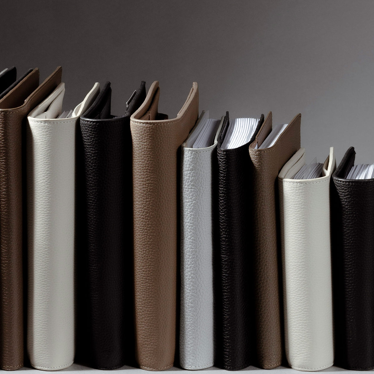 An image representing some of our Heirloom Premium Leather Folios. The different folios and colors are standing up side by side with their spines facing out against a gray background.