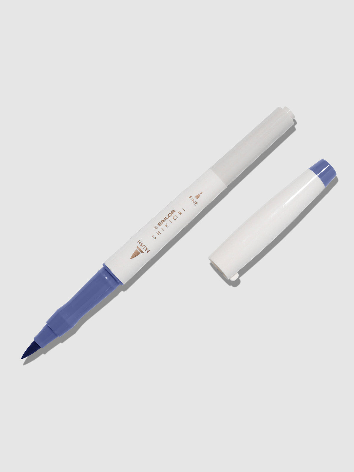 Brush pen displayed on a neutral background. It is uncapped with its brush nib exposed, and the cap lying parallel to the marker. Color pictured is Nioisumire.