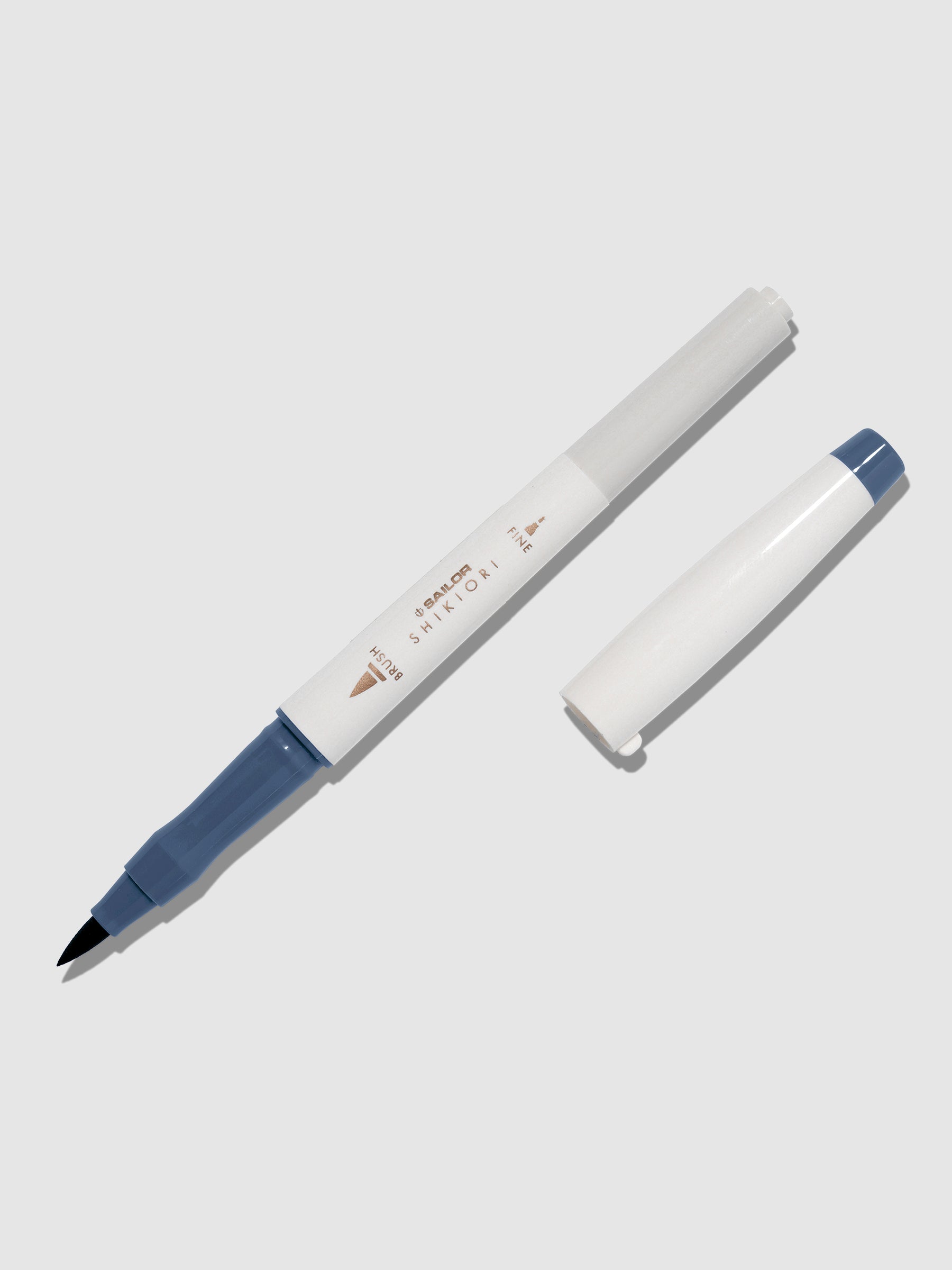 Brush pen displayed on a neutral background. It is uncapped with its brush nib exposed, and the cap lying parallel to the marker. Color pictured is Shimoyo.