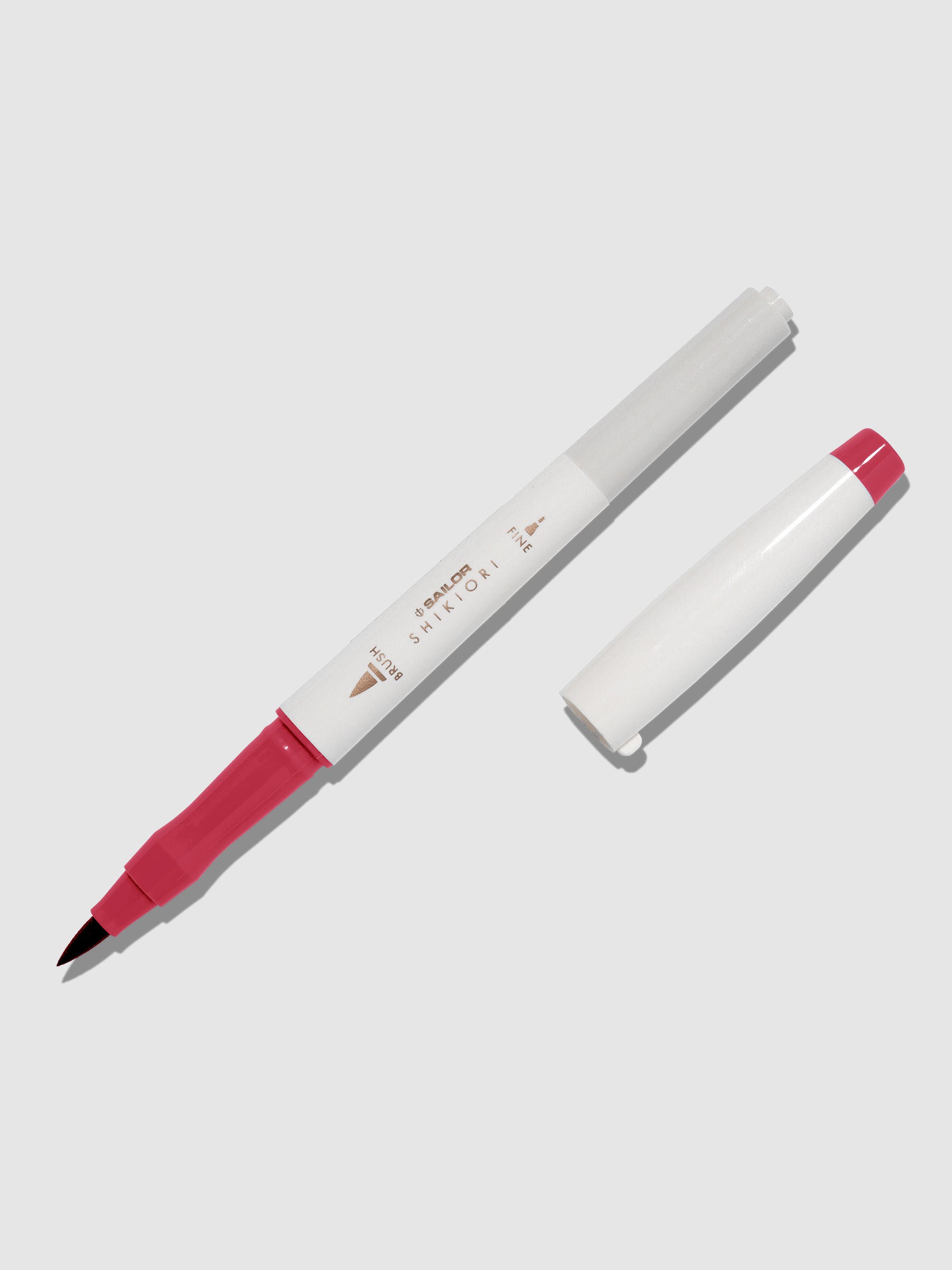 Brush pen displayed on a neutral background. It is uncapped with its brush nib exposed, and the cap lying parallel to the marker. Color pictured is Yodaki.
