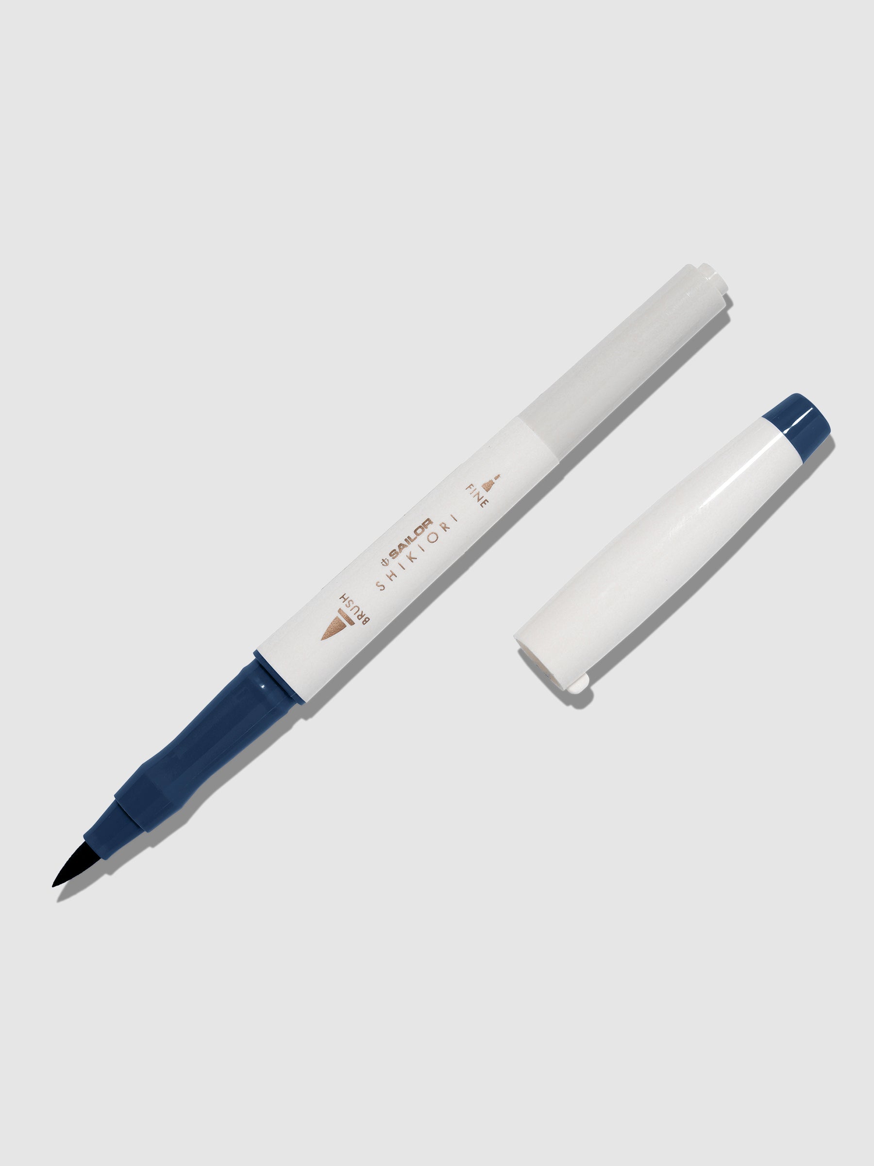 Brush pen displayed on a neutral background. It is uncapped with its brush nib exposed, and the cap lying parallel to the marker. Color pictured is Yonaga.