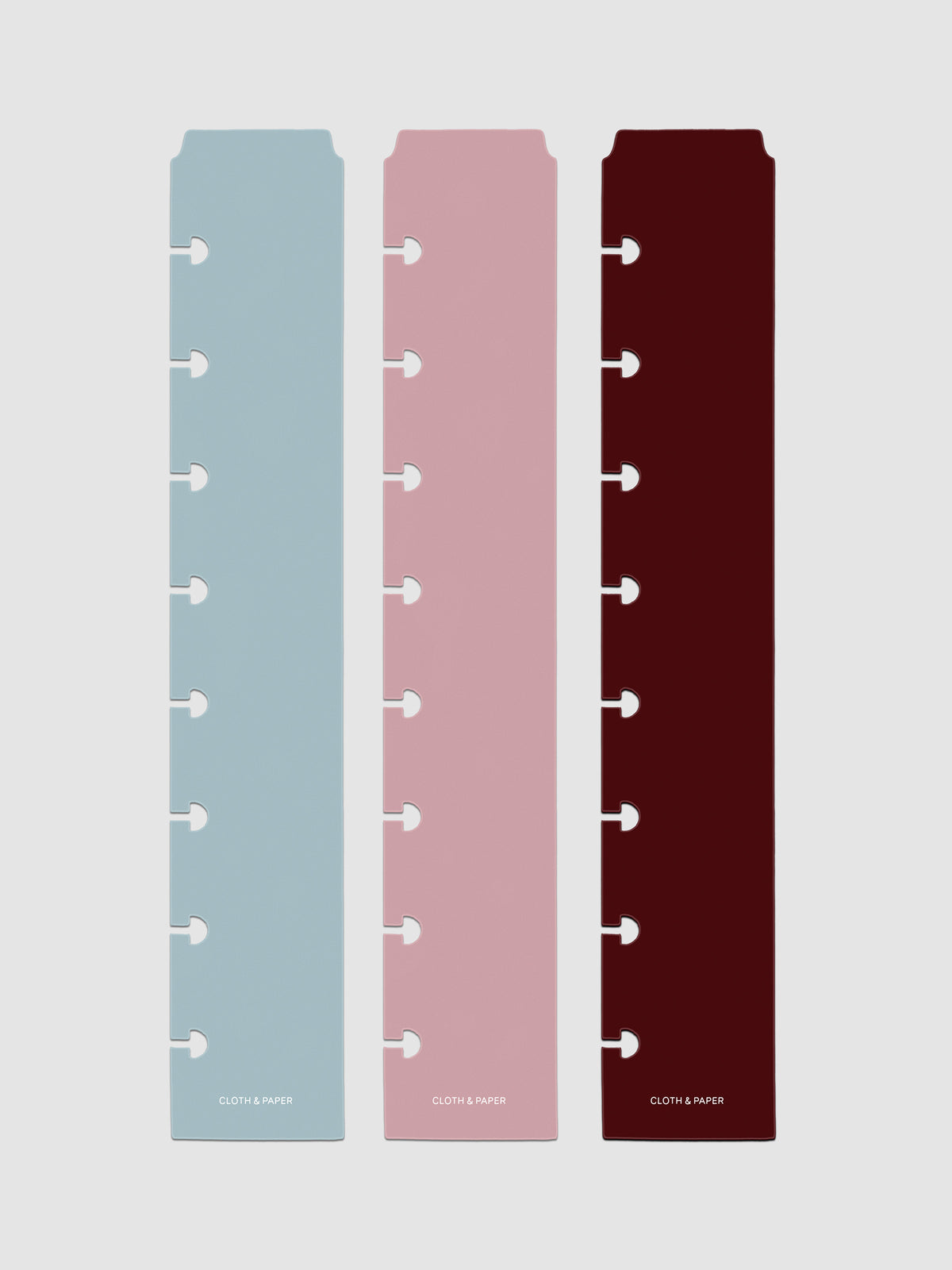 Set of three narrow page markers pre-punched for discbound planners in light blue, pink, and burgundy on a neutral background.
