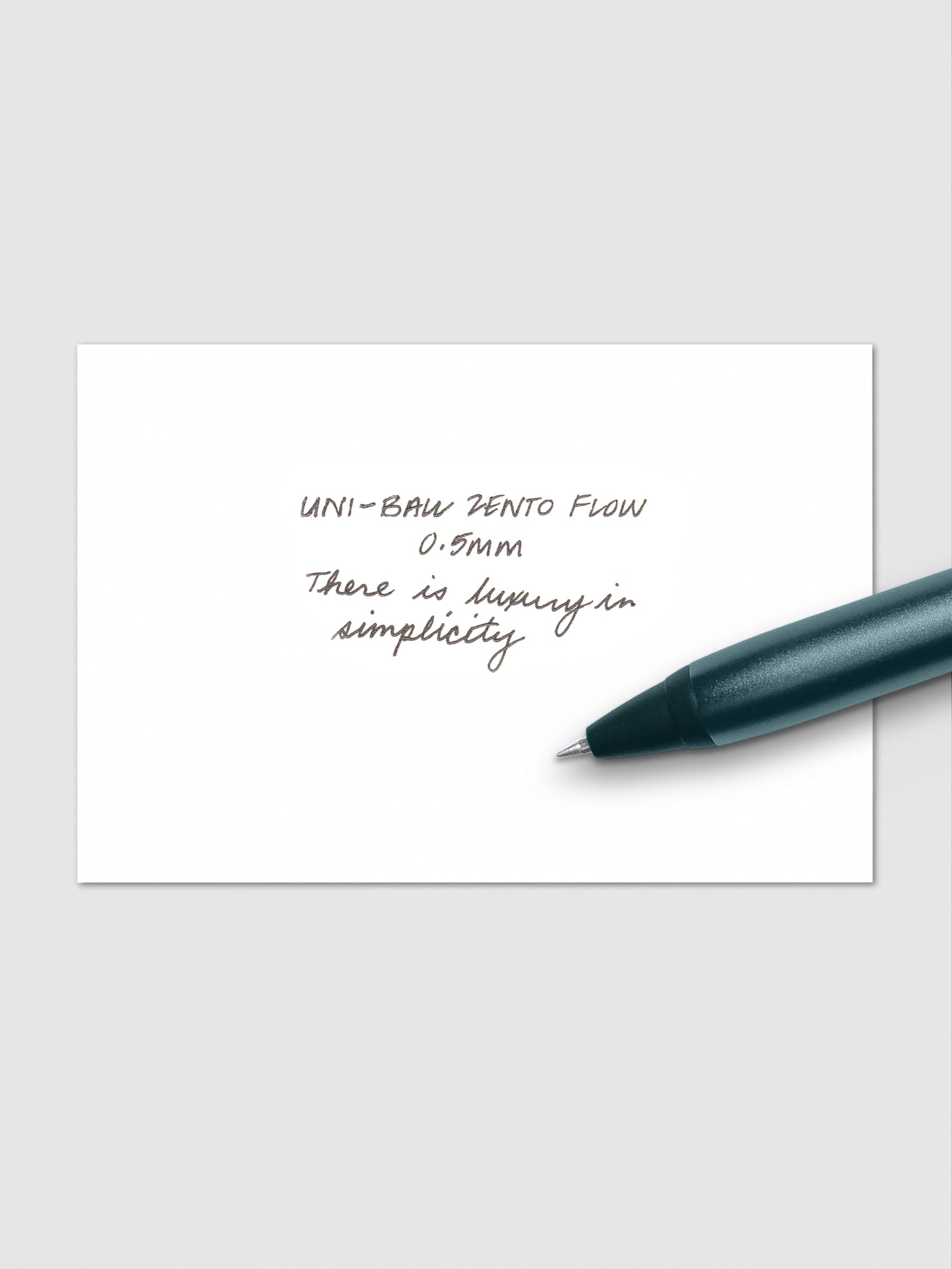 Handwritten writing sample using the Uni-ball Zento Flow Pen in a 0.5 mm nib. Shown with dark green-blue pen resting across paper.