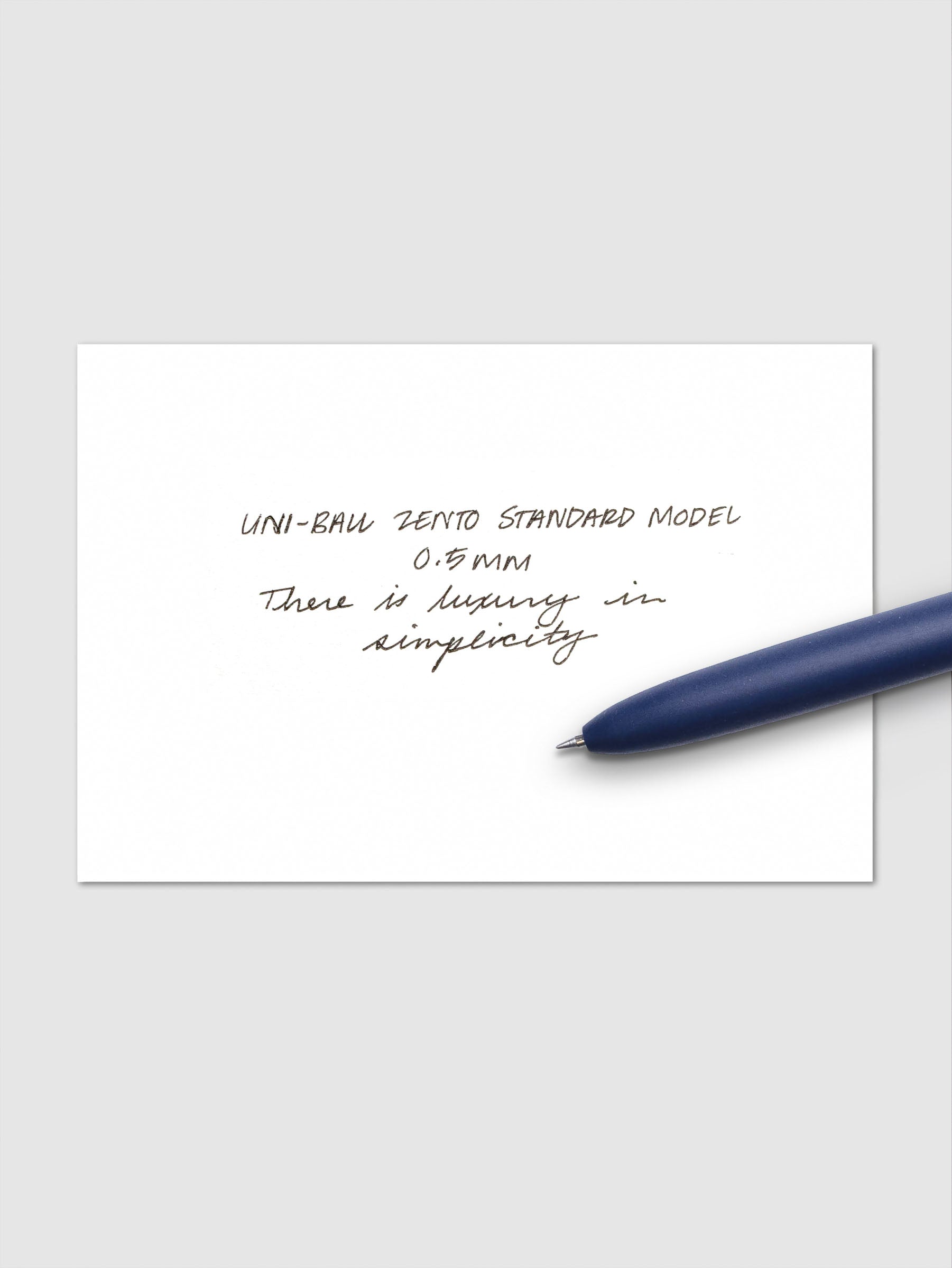 Handwritten sample using the Uni-ball Zento Standard Model Pen with black ink and a 0.5 mm nib. Shown with dark blue pen resting across paper.