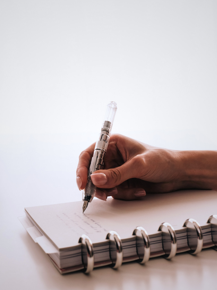 A hand writing on a Half Letter planner with silver planner discs using Platinum Curidas Fountain Pen. 