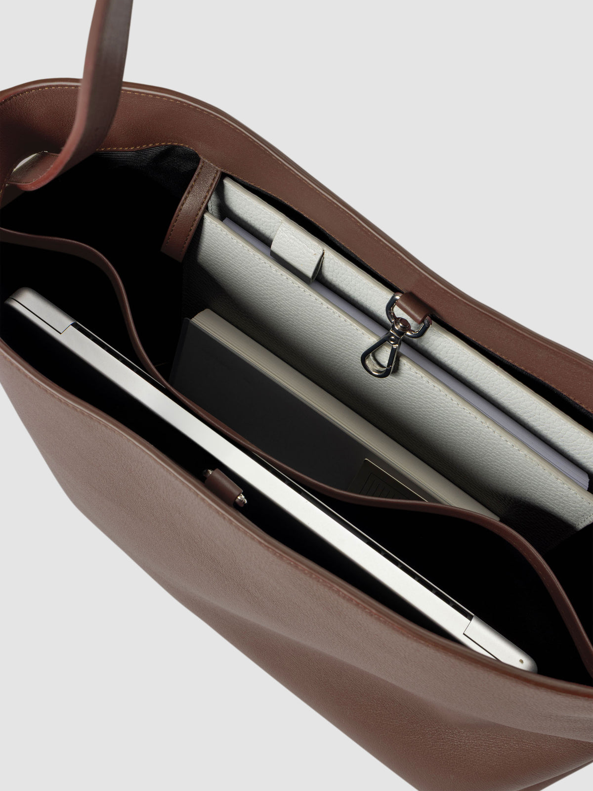 Detail view of a laptop and notebooks inside The Metro Tote in the color Cordoba.