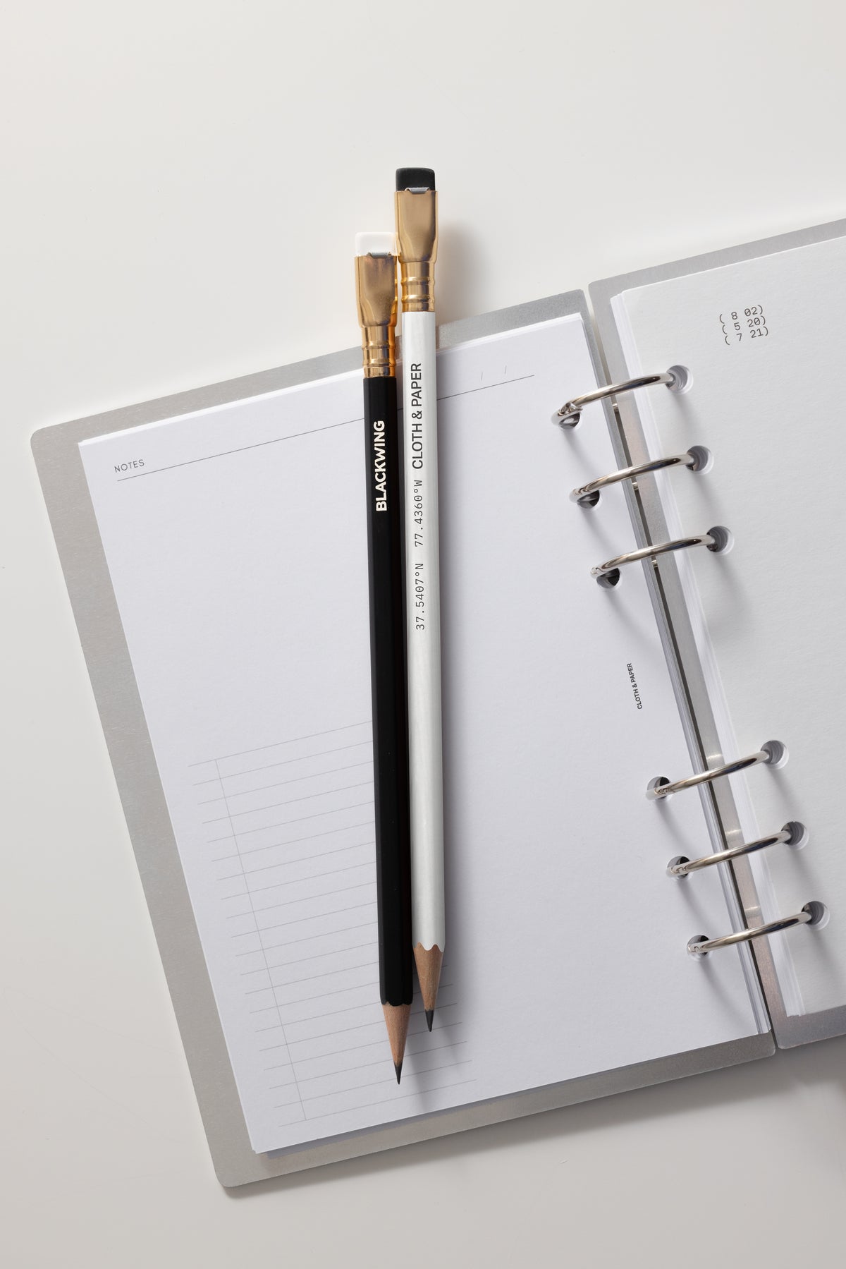 Open planner with a black pencil and white pencil on a light gray background