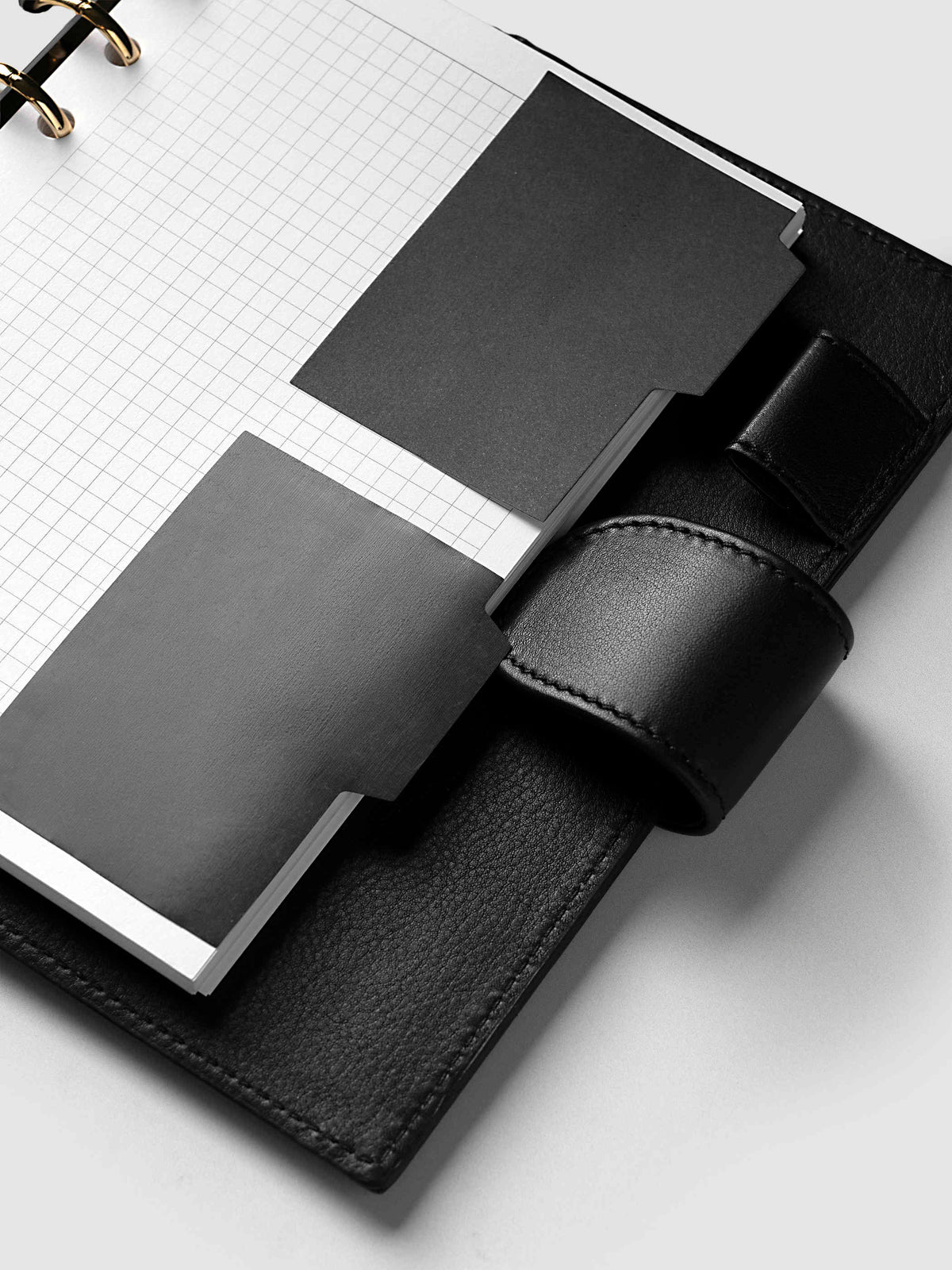 Blank Tab Sticky Note Set, Avant Garde, Cloth and Paper. Angled view of one transparent and one matte note on a grid insert, tabs tucked under the planner strap.
