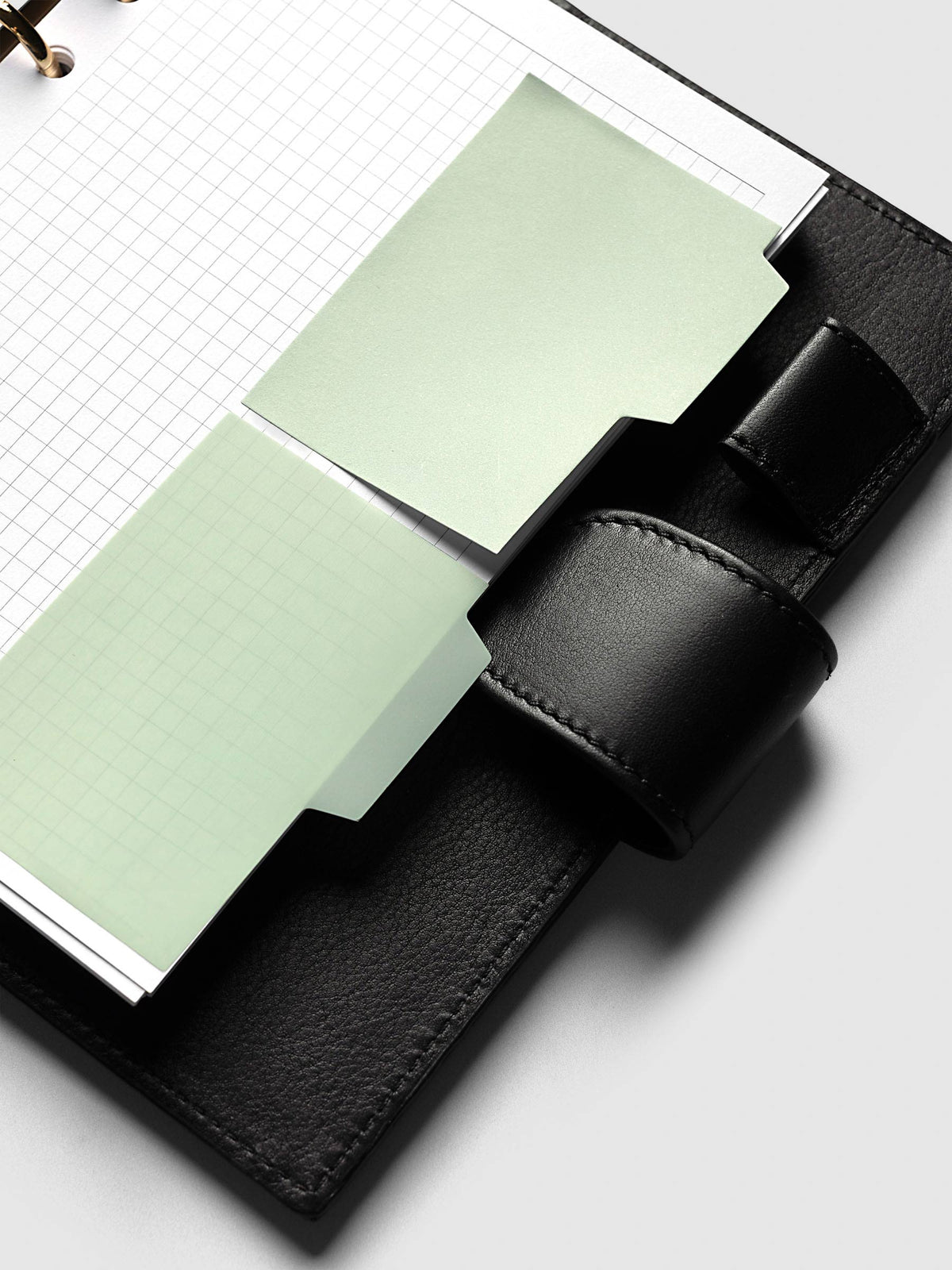 Blank Tab Sticky Note Set, Matcha, Cloth and Paper. Angled view of one transparent and one matte note on a grid insert, tabs tucked under the planner strap.