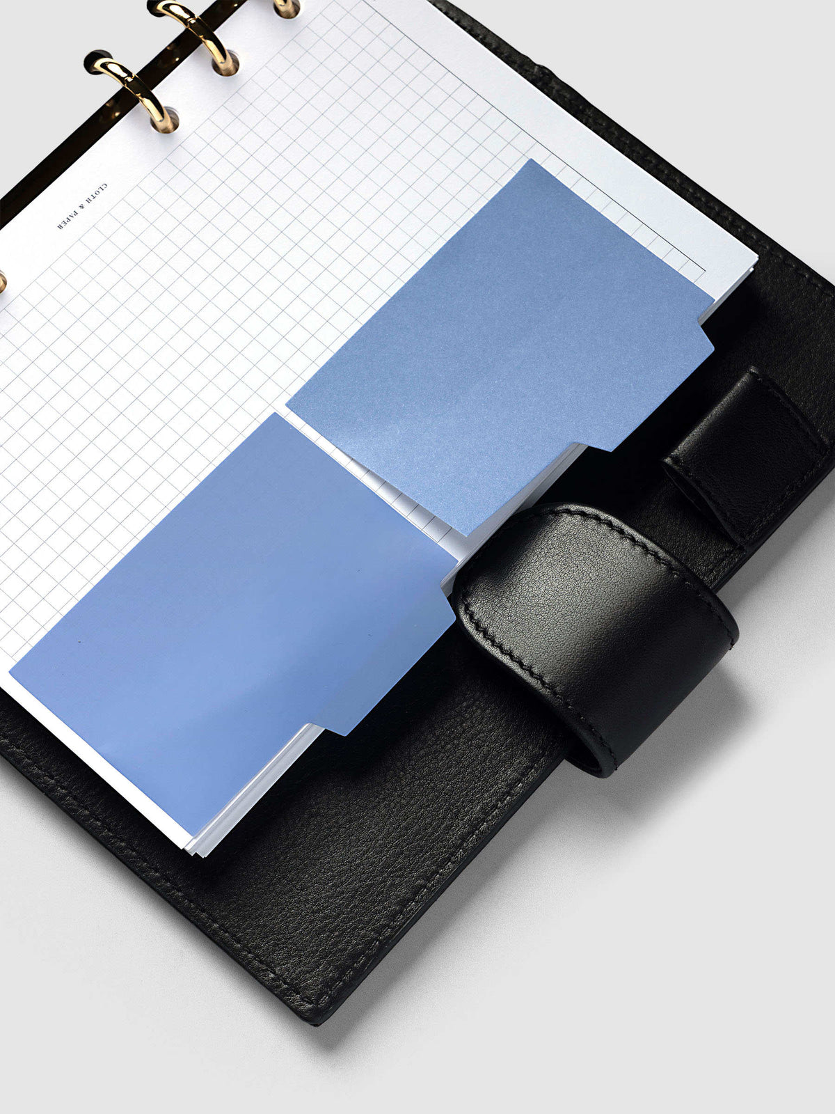 Blank Tab Sticky Note Set, Santorini, Cloth and Paper. Angled view of one transparent and one matte note on a grid insert on gold rings.