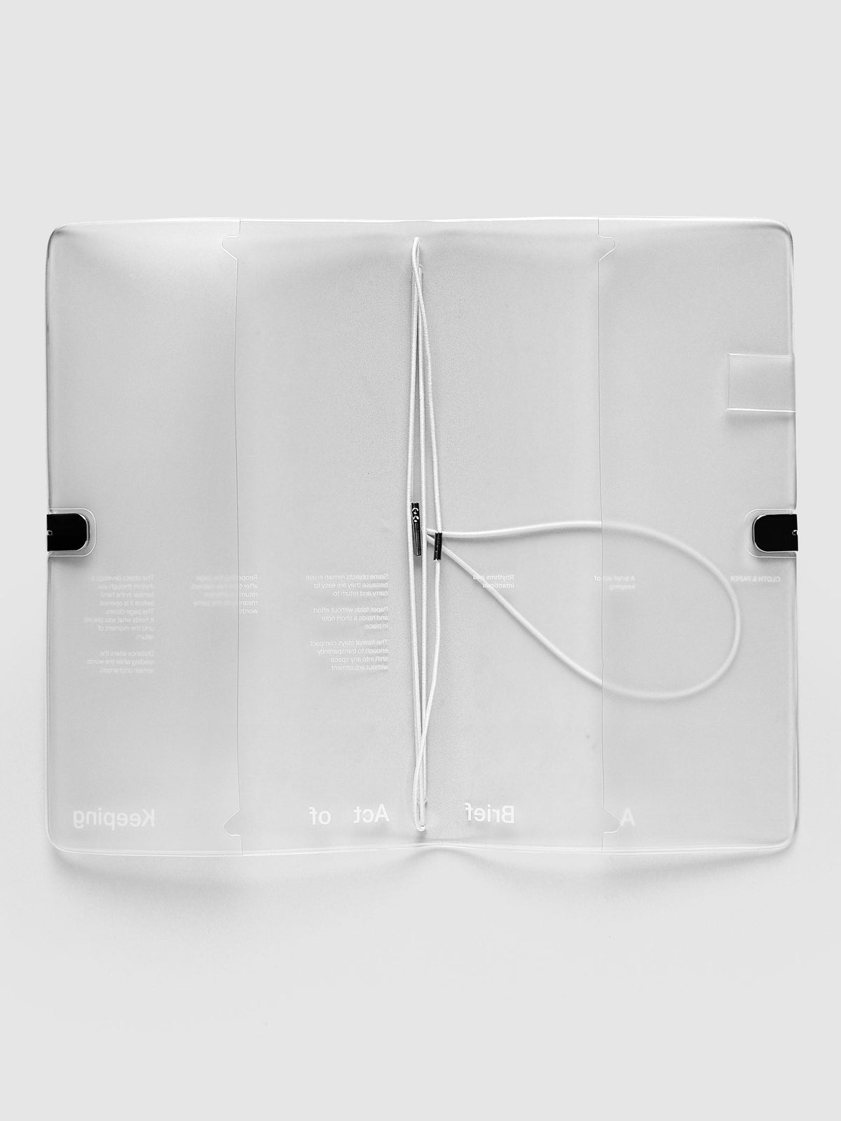 Act of Keeping Travel Cover, A5 Slim, open flat showing the white elastic insert bands with silver metal ends and A Brief Act of Keeping printed across the inside