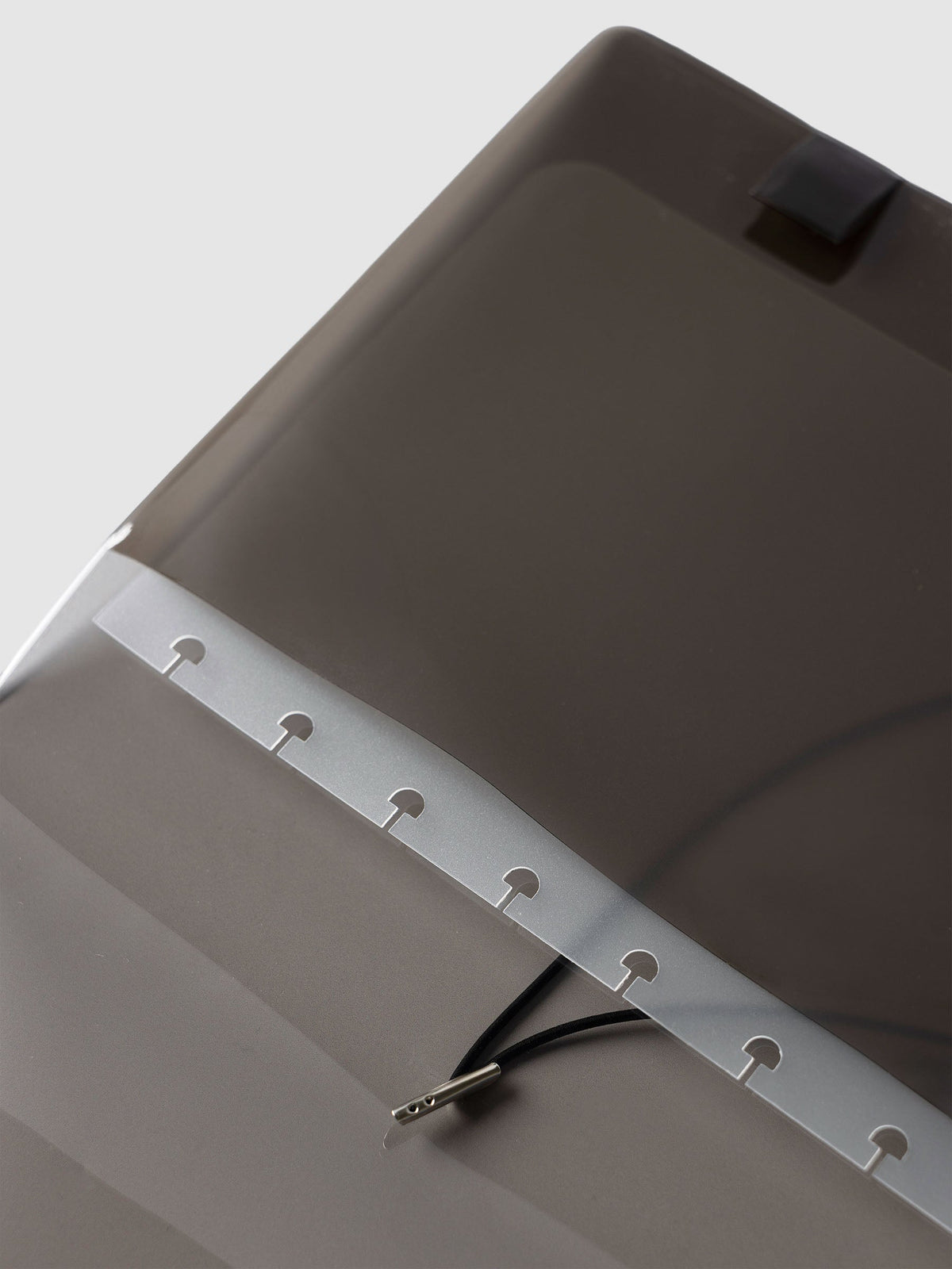 Close-up of the punched disc strip and black bungee cord with its silver metal end inside the black tinted vinyl Folio Cover