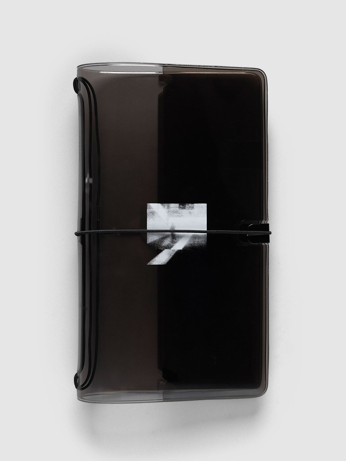 Image Duo Travel Cover, A5 Slim, in tinted black vinyl, closed with a black elastic cord across a white halftone photo print on the front