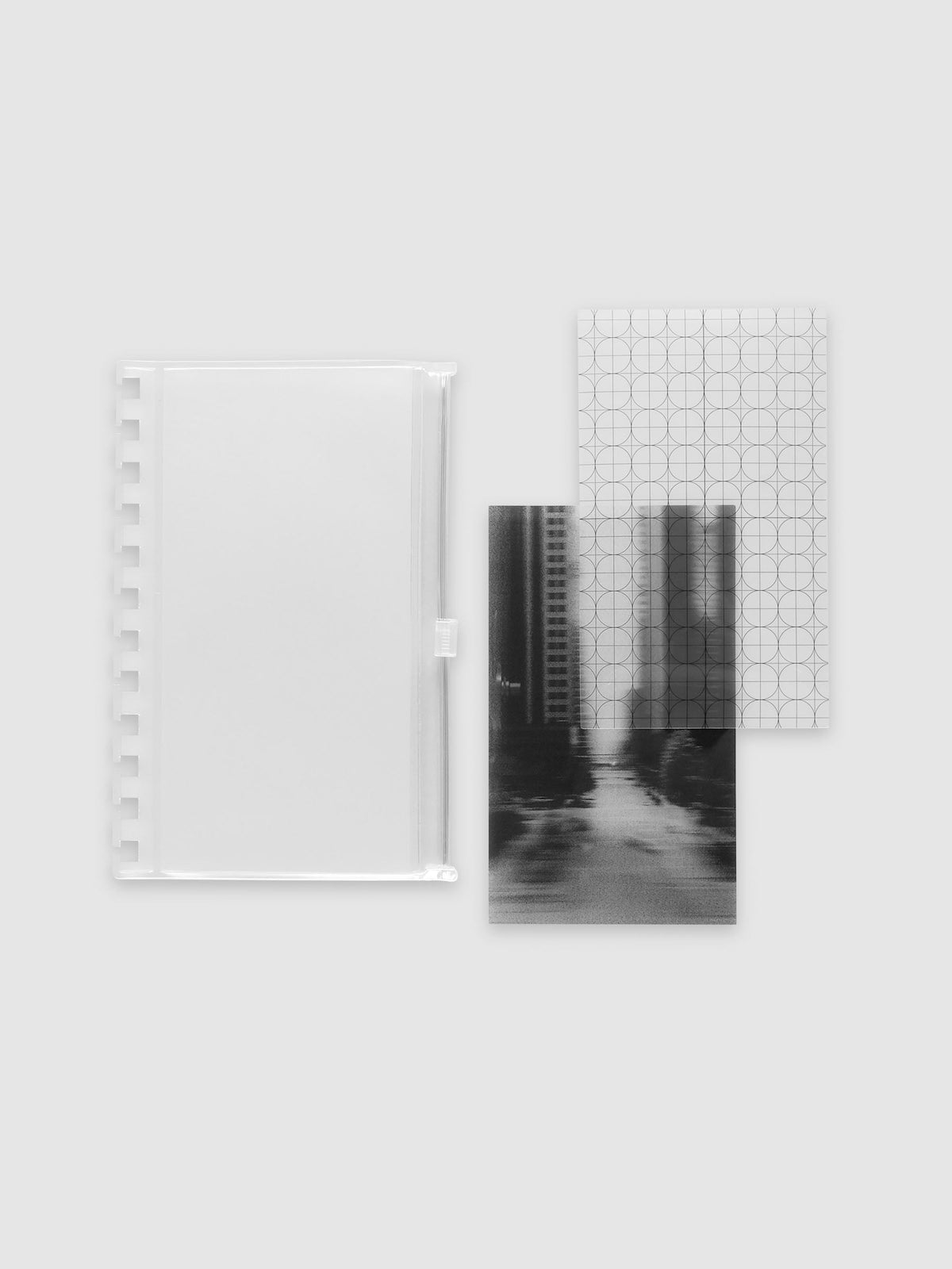 One frosted transparent zippered pouch, one clear circle and graph overlay and one black and white blurred photo insert laid side by side. Shown in size CP Petite Spiral.