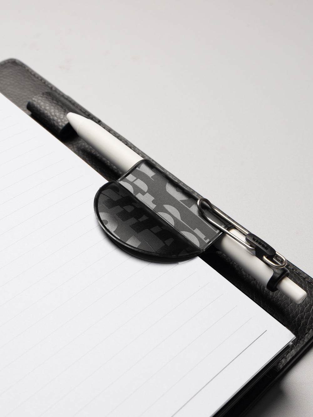 Black magnetic bookmark pen holder with spot gloss details shown holding a pen in a planner