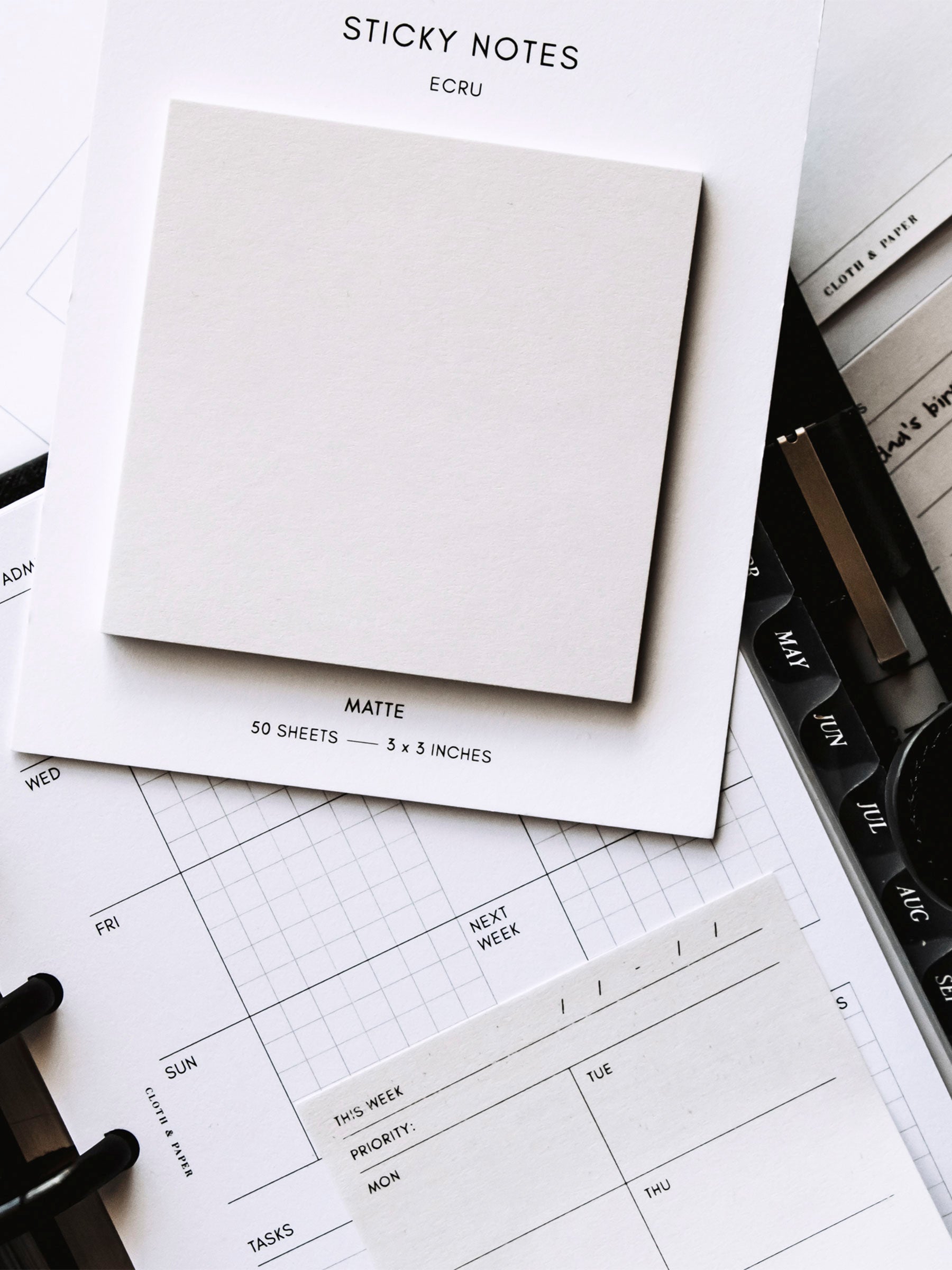 Pad of sticky notes on top of a discbound planner. The planner page has a sticky note printable stuck to it.