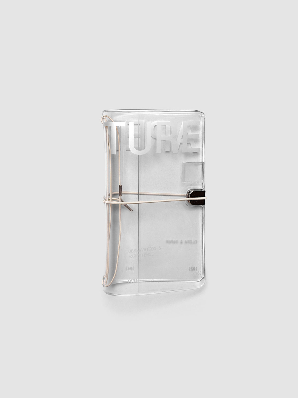 Aperture Travel Notebook Cover in Pocket Plus size, closed, in clear vinyl with silver typographic print and metal tab closure