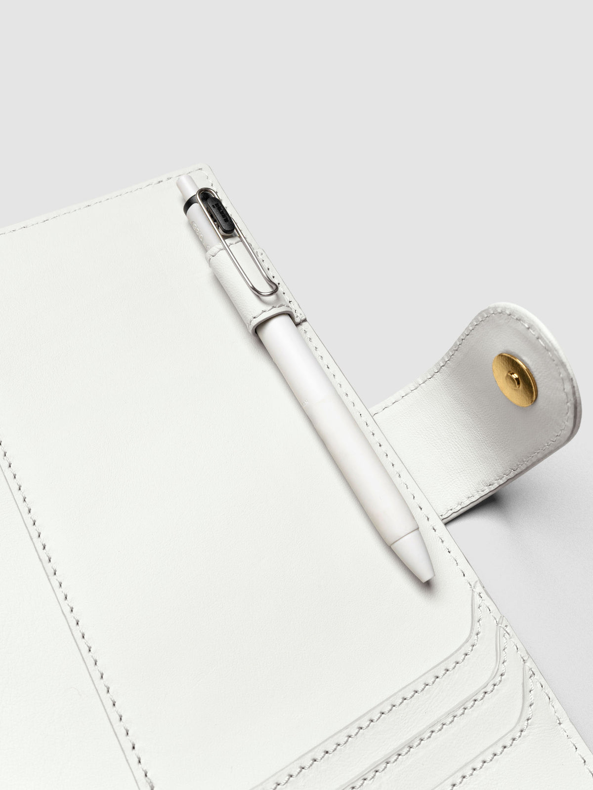 Detail of a pen threaded through the pen loop on the right interior of an off-white genuine leather A5 planner cover