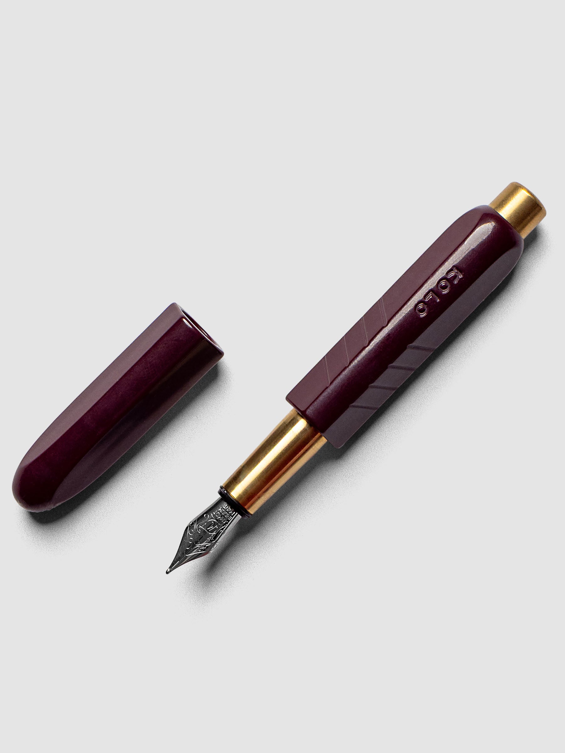 Kolo Tino Fountain Pen in the color Acrylic Cabaret, a deep burgundy barrel with brass accents and a silver medium nib shown with cap off.