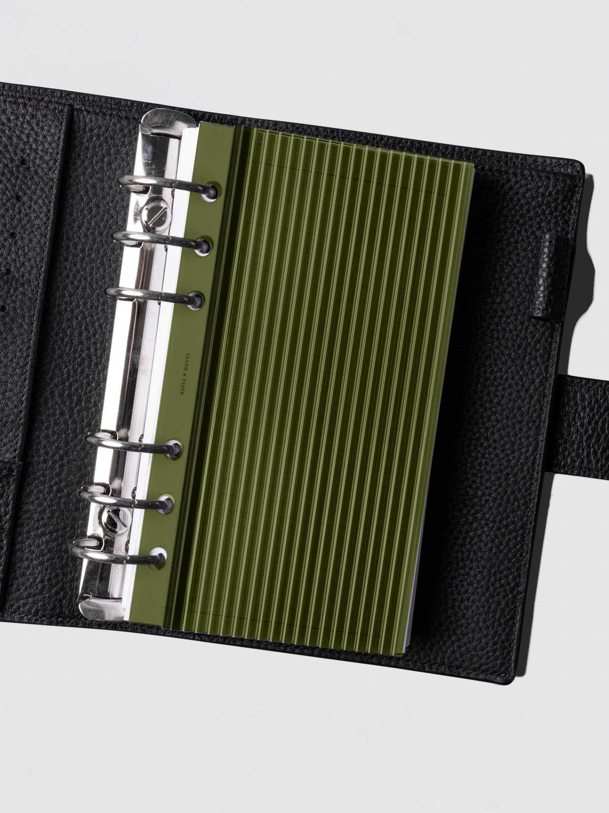 Olive fluted planner dashboard in Personal size shown in a black leather six ring agenda with silver rings.