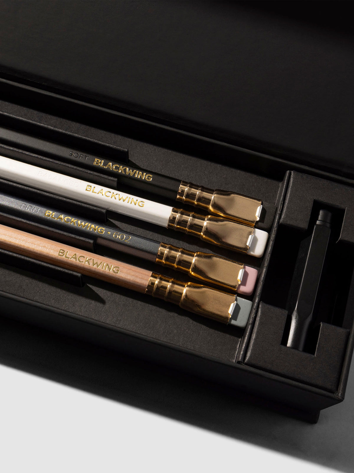 Closeup of four pencils and black point guard inside black storage box.