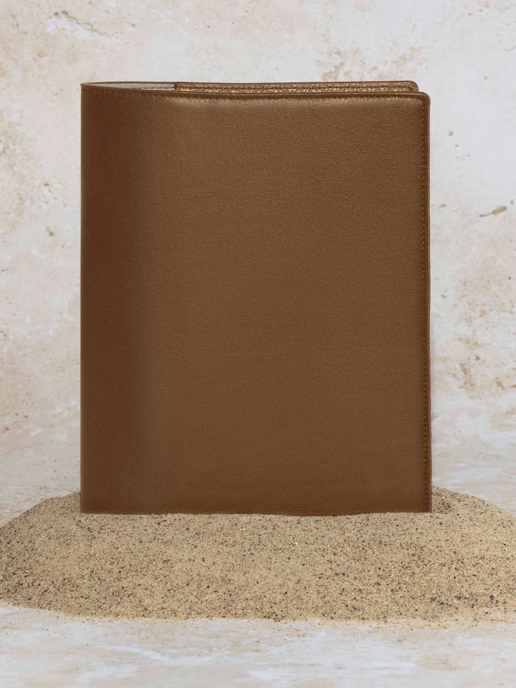 Folio displayed on a textured tan background, placed in a pile of sand. Color pictured is clay brown. 