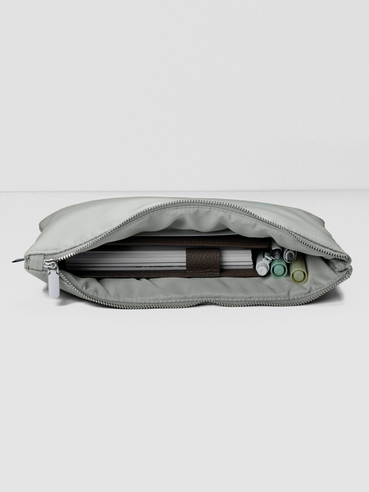 Light green-grey nylon, zippered, padded travel case shown laying down, open with a planner and writing accessories inside.