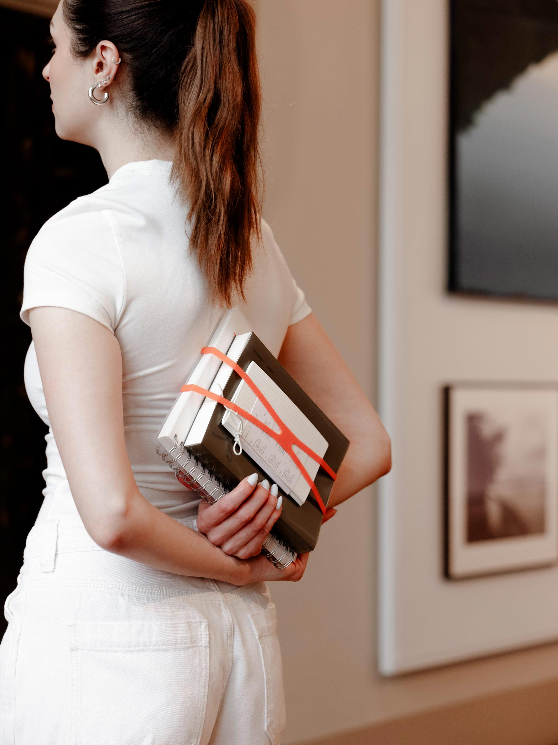 Woman holding set of three Commonplace notebooks behind her back.
