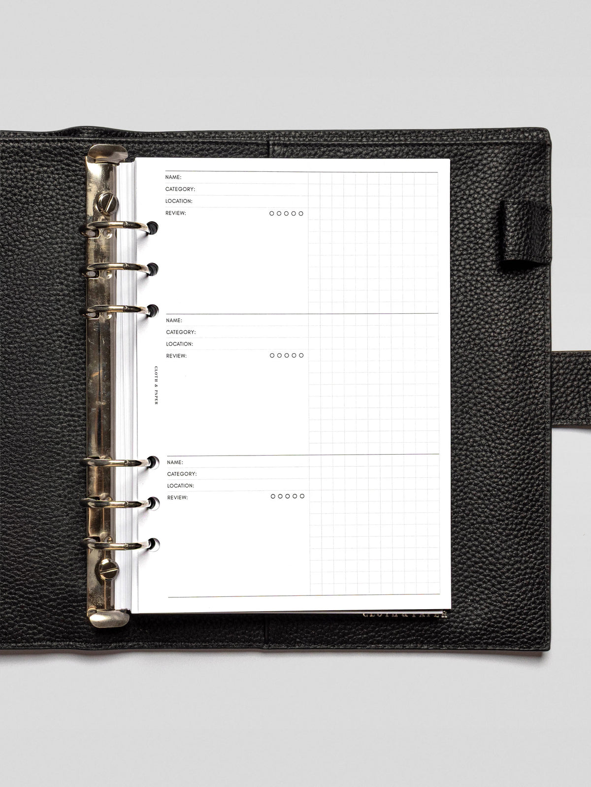 A close-up of the Experience Tracker Inserts in an open black leather planner binder, showing structured fields for Name, Category, Location, Review, and a 5-dot rating system, along with a right-hand grid section for notes.