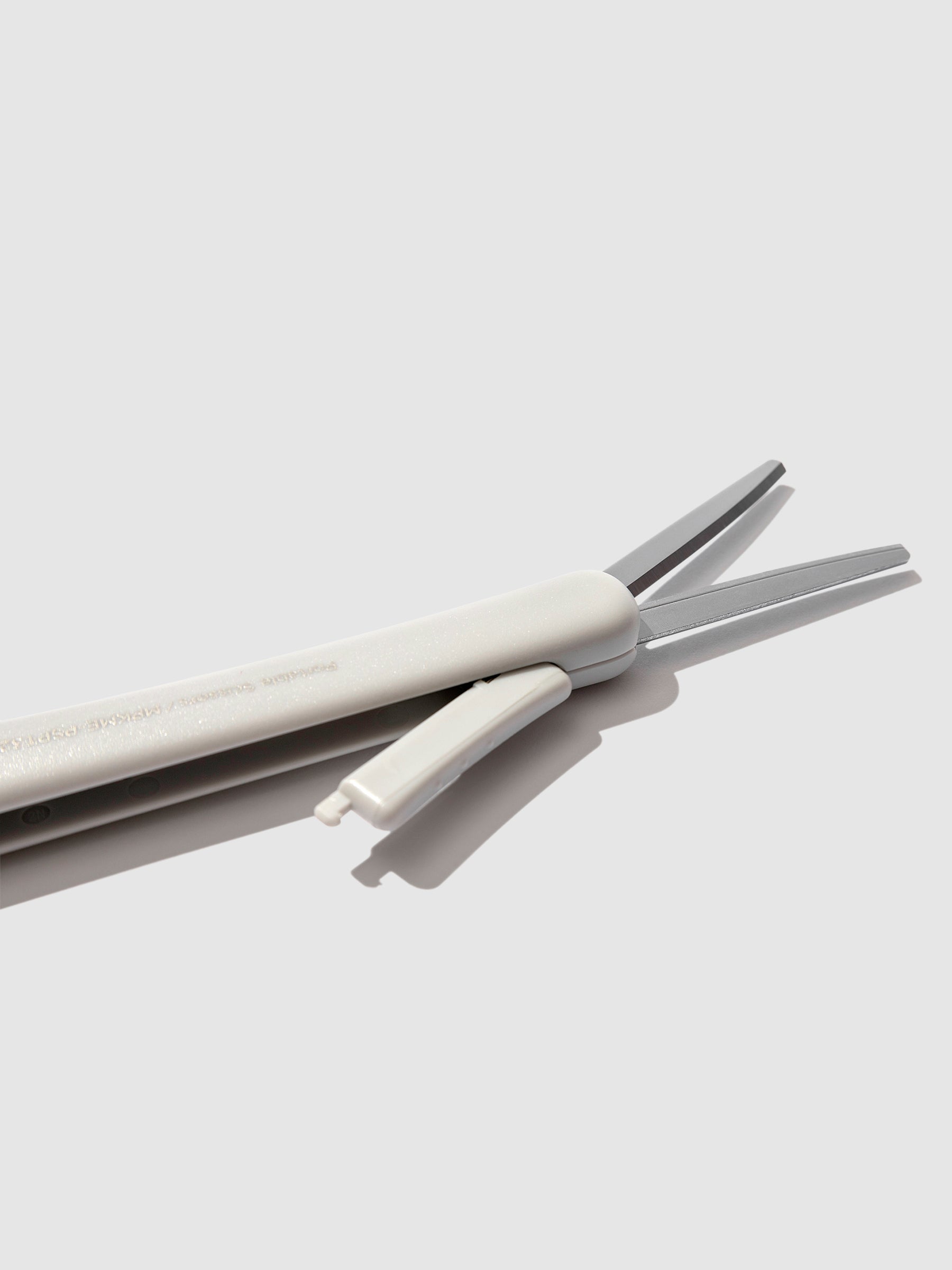 Closeup of scissors with blade exposed, showing the mechanism that exposes the scissor blades. Color shown is Grayish Ice. 