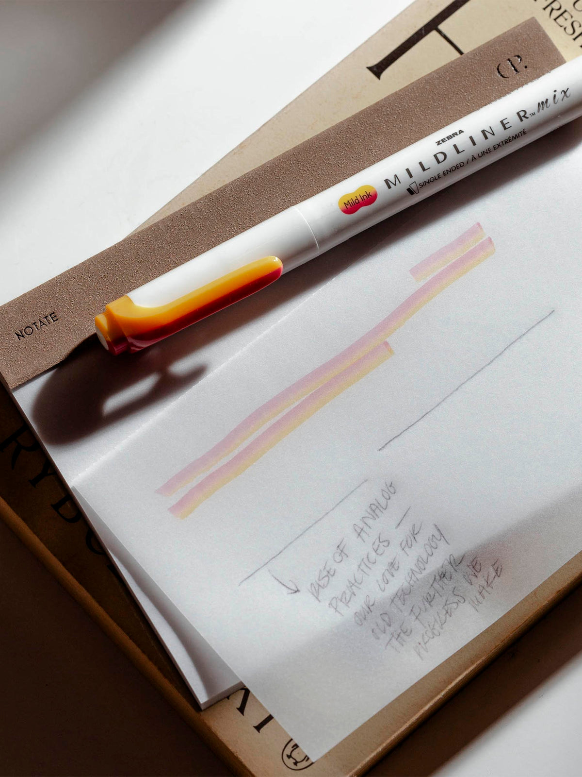 Notepad in use on a neutral background. One of the pages has been written on in pencil and highlighter.