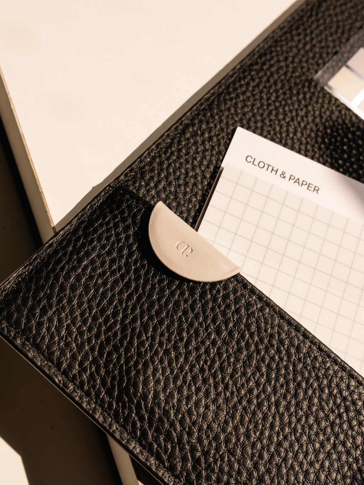 The Angora Mini eCLIPse bookmark clipped onto a leather planner pocket, holding a sheet of grid paper with the Cloth & Paper logo visible.