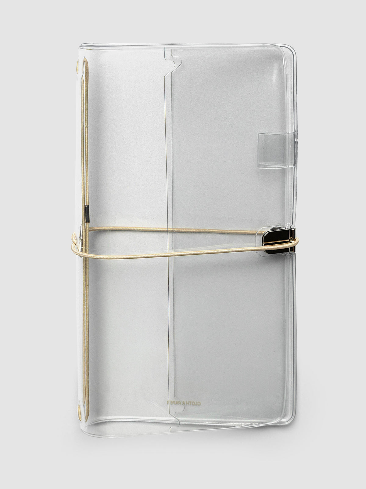 A clear acrylic notebook cover with a beige metal band closure, shown on a light gray background.