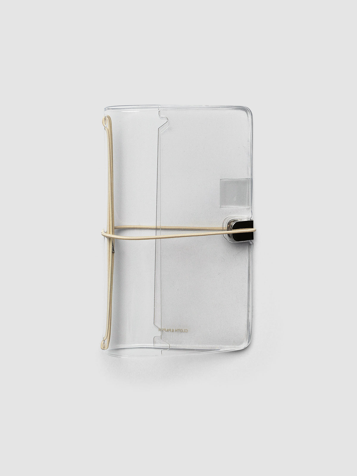 A clear acrylic notebook cover in Pocket Plus with a beige metal band closure, shown on a light gray background.