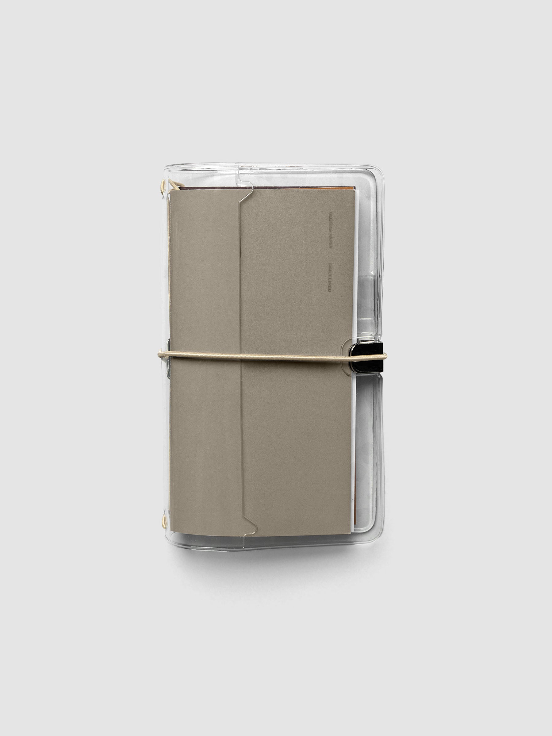 Clear Vinyl Travel Notebook Cover in Pocket Plus shown closed with a brown travel notebook inside, secured with a beige bungee closure.