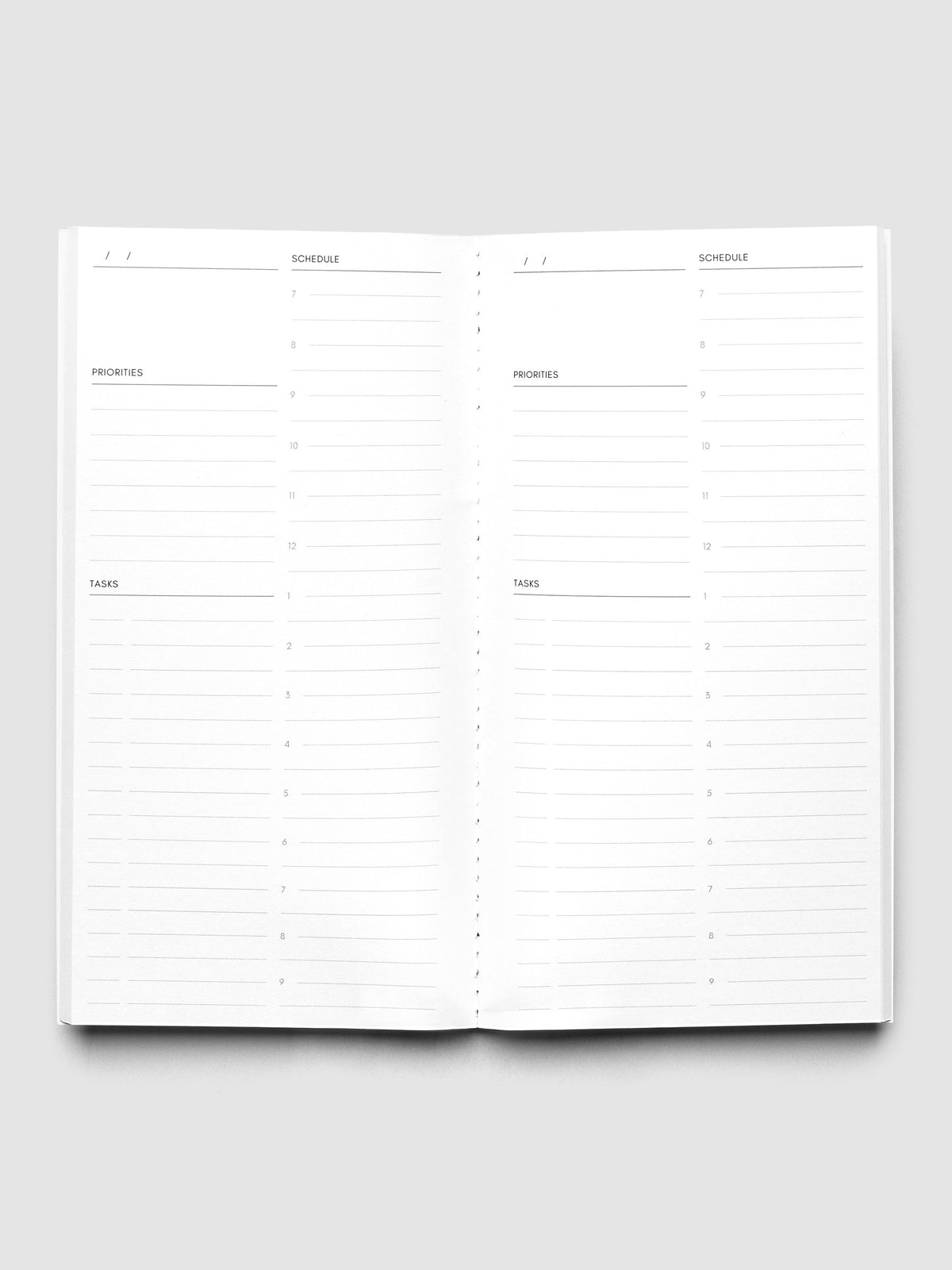 An open white daily planner or notebook showing lined sections for Monday through Sunday, with columns for priorities, tasks, and notes, photographed on a light gray background.