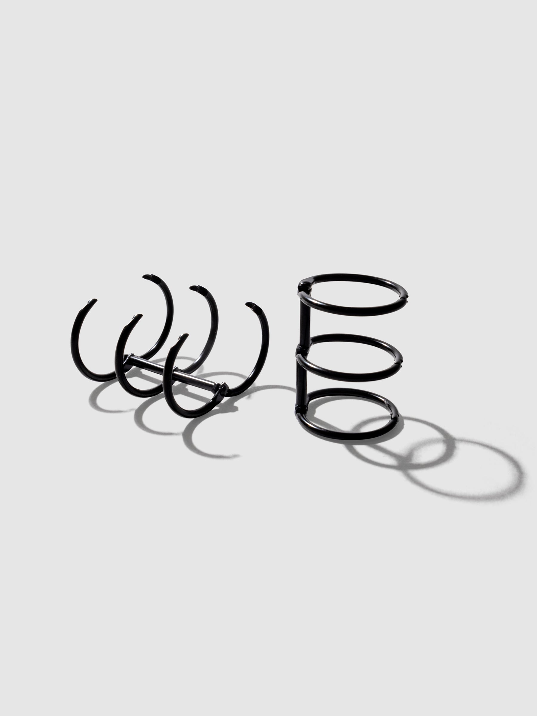 Black rings displayed on a neutral background. One set is laid on its back and opened, the other is sat upright with rings closed.