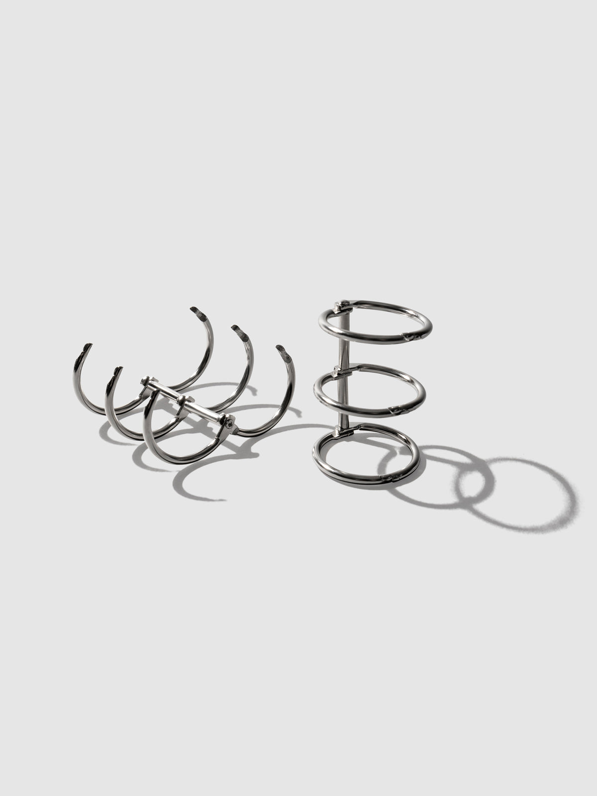 Silver rings displayed on a neutral background. One set is laid on its back and opened, the other is sat upright with rings closed.