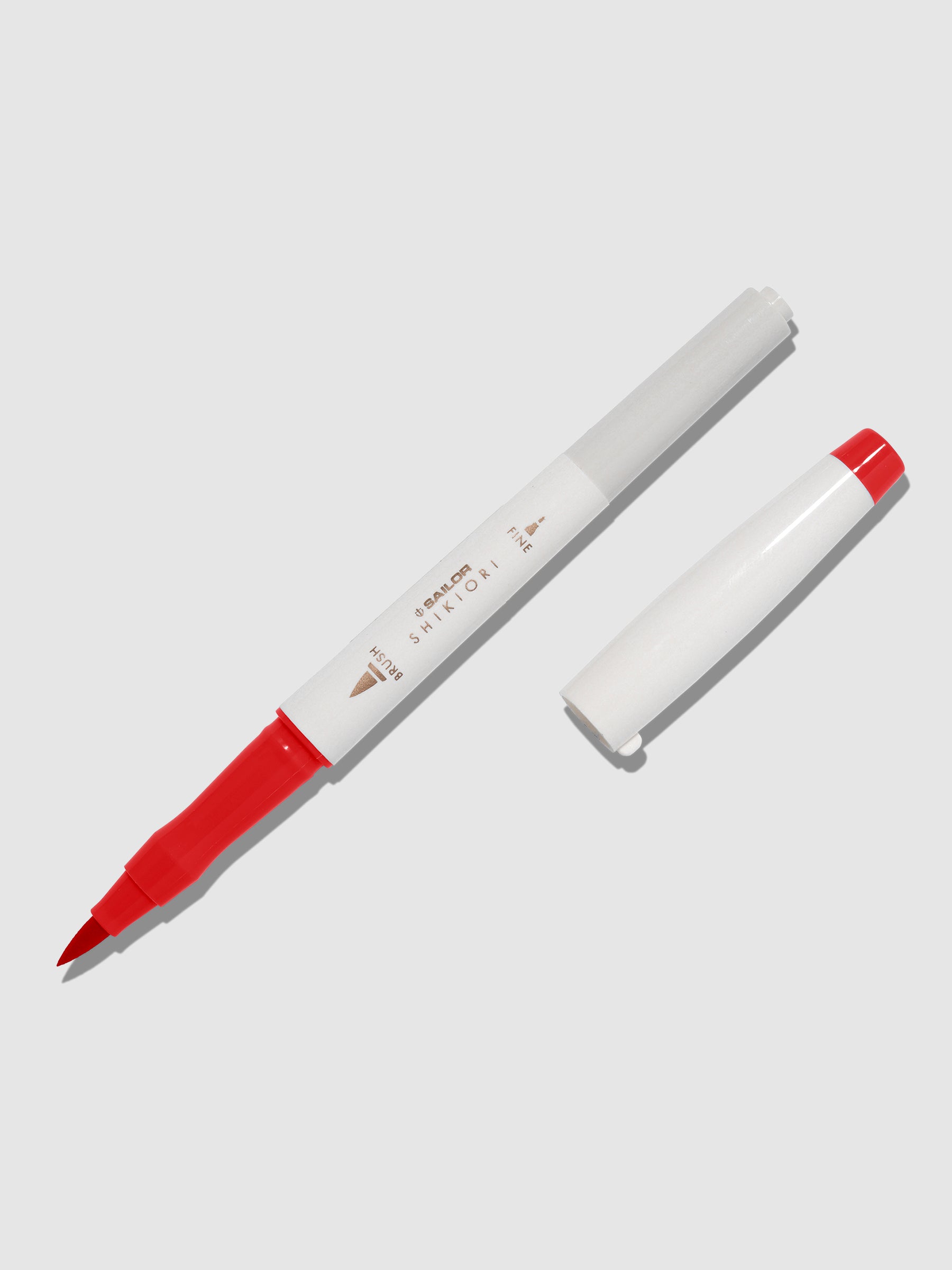 Brush pen displayed on a neutral background. It is uncapped with its brush nib exposed, and the cap lying parallel to the marker. Color pictured is Irori. 